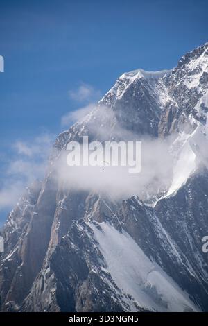 Dramatic mountain scene with lone paraglider crossing low cloud over rocky peak Stock Photo