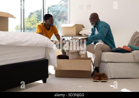Unpacking clothes African American father and son folding blankets in sunny room with moving boxes Stock Photo