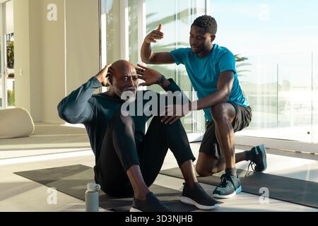 Coaching African American men performing sit-ups in home gym, with exercise mats and water bottle Stock Photo