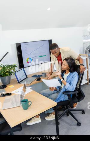 Reviewing African American colleagues analyzing reports at office desk, with mounted monitor Stock Photo