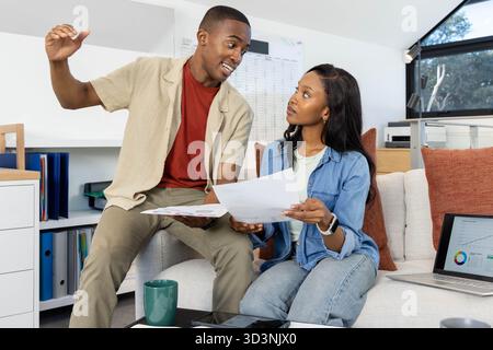 African American couple analyzing printed documents in home office, with coffee mug and laptop Stock Photo