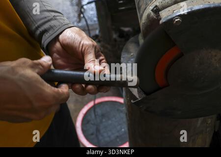Focused worker hands sharpening metal tool on grinding machine in workshop. Close up of craftsman at work, using grinder for precision and skill in ma Stock Photo