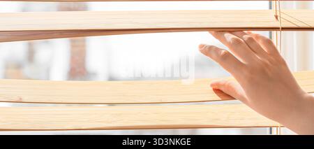 Hand of woman separating slats of blinds and looking through window, closeup Stock Photo
