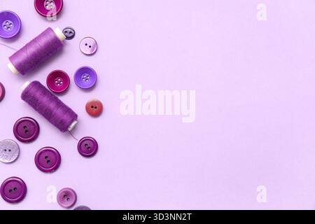Different buttons and thread spools on lilac background Stock Photo