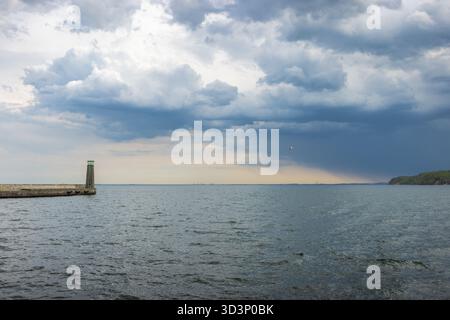 The coast of the Baltic Sea in northern Poland. Seascape: lighthouse stands against dramatic sky, calm water reflecting light, capturing a serene mome Stock Photo