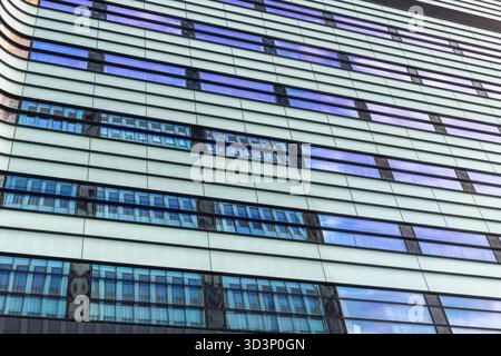 A modern building with a sleek design featuring repeating horizontal lines and reflecting blue sky in the multiple windows, from a low angle. Stock Photo