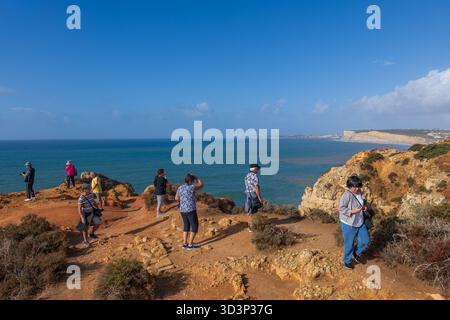 Group of tourists standing on edge of a cliff, people enjoy the view of scenic coastline of Algarve region by the Atlantic Ocean in Lagos, Portugal. Stock Photo