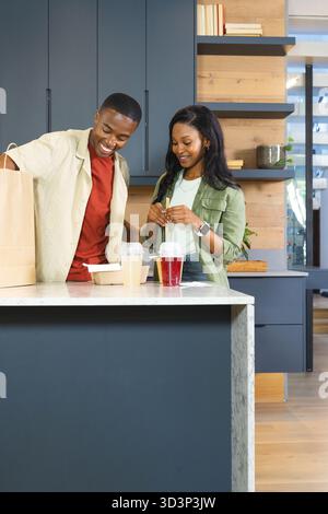 African American couple unpacking grocery bag in kitchen, with drink cups on marble island Stock Photo