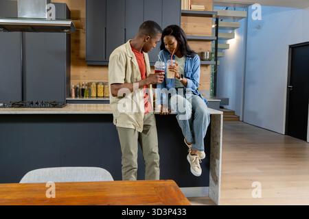 African American couple drinking smoothies at modern kitchen island, with plastic smoothie cups Stock Photo