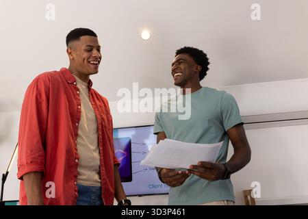 Discussing details, Diverse male coworkers conversing in office with monitor and printed documents Stock Photo