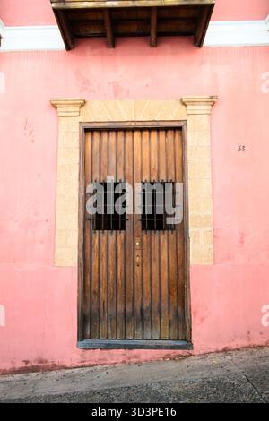 A wooden door with iron bars on its windows is set into a pink wall with a light stone frame. The building facade has a classic architectural style. Stock Photo