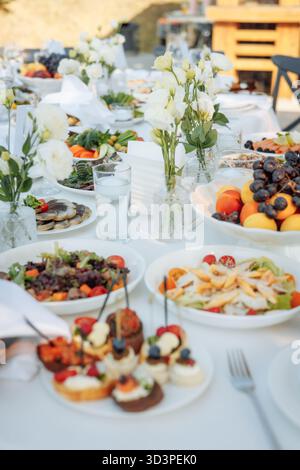 Sunlit wedding table with floral centerpieces, fresh salads and elegant canapes Stock Photo