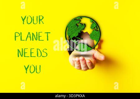 Hand holding a globe with the words Your planet needs you written below it. Concept of urgency and responsibility towards the environment, encouraging Stock Photo