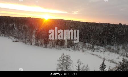 Sunset over snowy forest and frozen lake aerial winter view Stock Photo