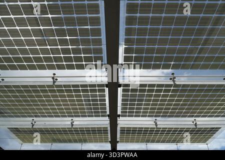 Solar panels. The underside of several outdoor solar panels reveals their grid-like structure and mounting framework, with blue sky and clouds visible Stock Photo