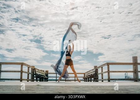 Young woman dancing with flowing fabric on pier Stock Photo