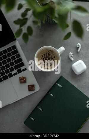 Top view of a cozy home workspace, featuring a laptop, coffee cup, notebook, and wireless earbuds. The setup inspires productivity and relaxation for Stock Photo