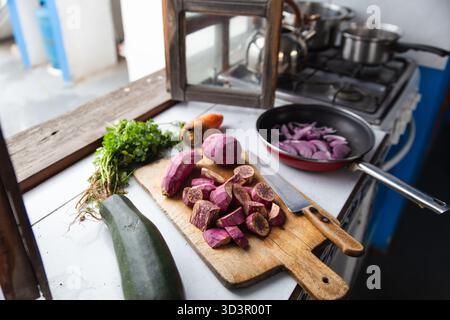 A vibrant kitchen scene showcasing freshly chopped vegetables on a wooden cutting board beside a knife, with a pan of sliced onions near a stove, exud Stock Photo