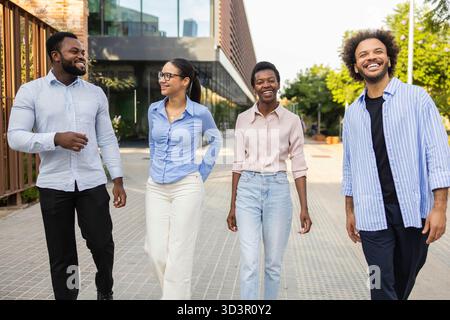 A diverse group of business professionals joyfully walking together in an urban setting, showcasing teamwork and positivity in a dynamic city environm Stock Photo