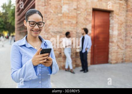 A diverse group of business professionals having a conversation outside a modern city office. One individual is using a smartphone, while others engag Stock Photo