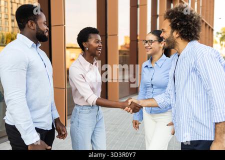 A diverse business team of professionals meets in an urban setting, exchanging handshakes and smiles, symbolizing teamwork, collaboration, and corpora Stock Photo
