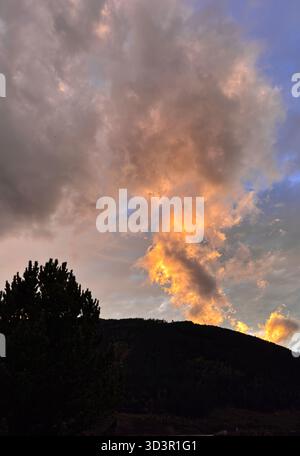 Golden sunset clouds drift above the dark silhouette of the Austrian Alps, creating a dramatic contrast in the sky, highlighting the natural beauty of Stock Photo