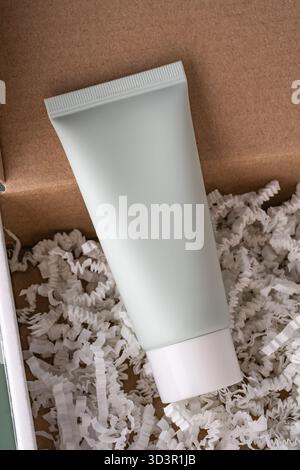 Top view of a white cosmetic cream tube nestled in shredded paper, set against a natural brown textured background, offering an aesthetic and eco-frie Stock Photo