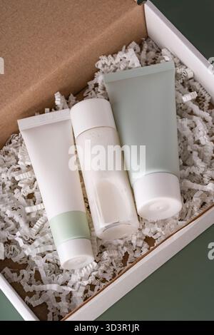 Top view of three cream tubes arranged in a box filled with white shredded paper. The setting has a green background, creating a minimalist and elegan Stock Photo