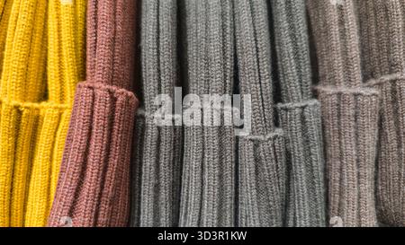 A variety of knit hats in vibrant colors, including yellow, brown, and gray, are neatly stacked in horizontal rows. The texture of the fabric emphasiz Stock Photo