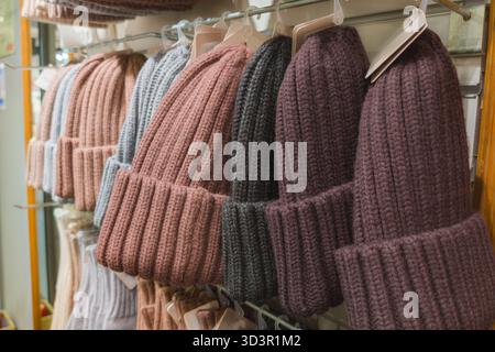 A variety of cozy knit winter hats are neatly displayed on store shelves. The hats come in multiple colors, including pink, gray, and purple, perfect Stock Photo