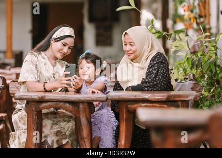 A joyful moment shared by three generations of a Muslim family in Southeast Asia, with a grandmother, mother, and daughter sitting together and smilin Stock Photo