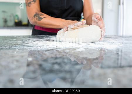 A woman skillfully kneads dough on a floured countertop, preparing to bake homemade bread in a cozy kitchen setting, embodying the art and tradition o Stock Photo
