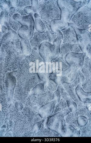 Abstract close-up of icy texture displaying organic, fluid shapes formed by frost on a surface. The image features subtle gradients of blue and gray, Stock Photo