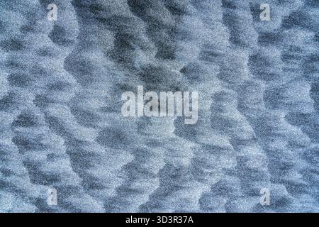 An abstract close-up view of rippled sand patterns, creating a mesmerizing texture. The natural blue-gray hue evokes a sense of tranquility and organi Stock Photo