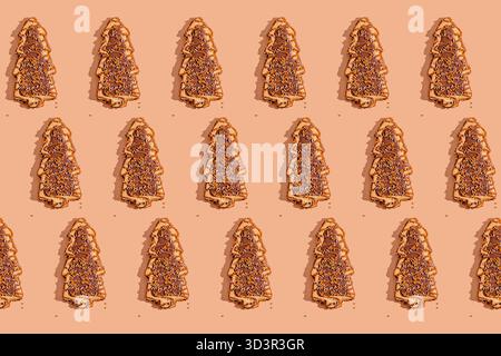 A pattern of gingerbread cookies shaped like Christmas trees with chocolate topping and sprinkles arranged on a beige background, casting neat shadows Stock Photo