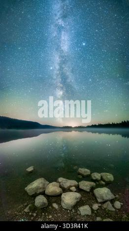 A captivating night scene of the Milky Way reflected over a calm mountain lake. The clear sky and distant horizon create a breathtaking view of nature Stock Photo