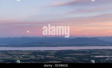 Serene view of a sunset over Lake Geneva, with a radiant sky reflecting vibrant hues of pink and orange. The tranquil waters complement the picturesqu Stock Photo