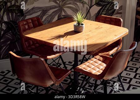 A stylish restaurant interior featuring a wooden table with four brown leather chairs. The setting is complemented by a small potted plant and a patte Stock Photo