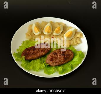 A plate with two fried meat patties on a lettuce leaf, mashed potatoes and a sliced ​​boiled egg. View from above, flat lay. Stock Photo