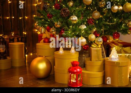 Cozy Christmas studio featuring a decorated tree with gold and red ornaments. Golden gift boxes, a red lantern, and warm fairy lights create a charmin Stock Photo