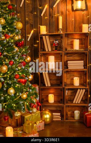 A cozy studio interior decorated for Christmas and New Years. with a lit Christmas tree adorned with red and gold ornaments, gifts, candles, and a boo Stock Photo