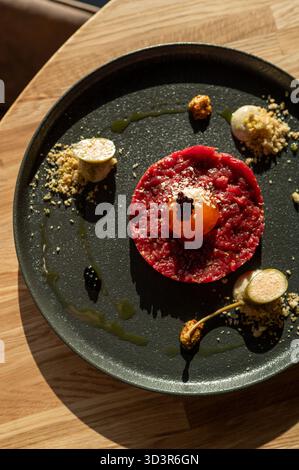 Elegant beef tartar garnished with a marinated egg yolk and dotted with balsamic caviar, presented on a dark plate for a gourmet dining experience. Stock Photo