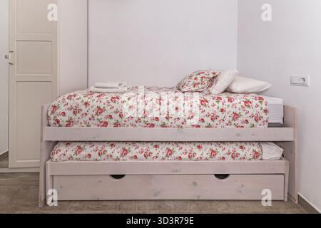 A composition of a small bedroom where a bed with built-in drawers features a light blue linen duvet, optimizing the available space. Stock Photo