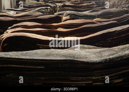 Hemayetpur, Bangladesh - 04 August 2021: View of stacks of cured leather, their rough, dark surfaces layered in a textured display of raw industrial m Stock Photo