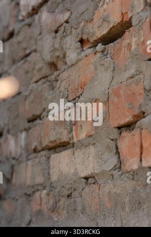 Close-up of a brick wall under construction, showing uneven mortar and exposed orange bricks. Textured surface conveys urban, industrial, renovation aesthetics. Vertical photo, selective focus.  Stock Photo