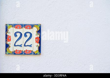 Twenty-two house number on decorative ceramic tile and white wall. Stock Photo