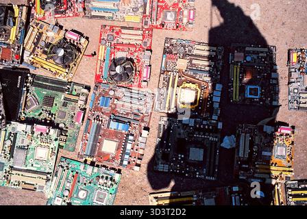 Printed circuit boards from old computers lie on concrete at a market, photographer’s shadow crossing them, captured in analog snapshot. Stock Photo