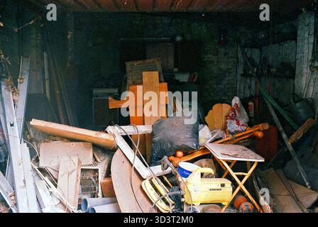 An old garage filled with chaotic piles of forgotten items, dust settling over a jumble of tools, boxes, and memories. Stock Photo
