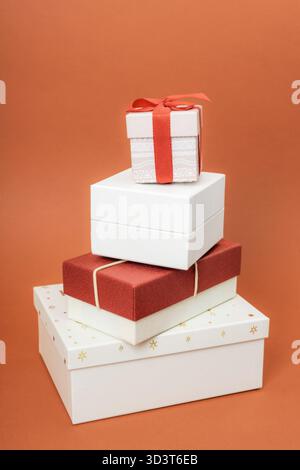 Stacked Christmas gift boxes with a red ribbon on orange background. Stock Photo