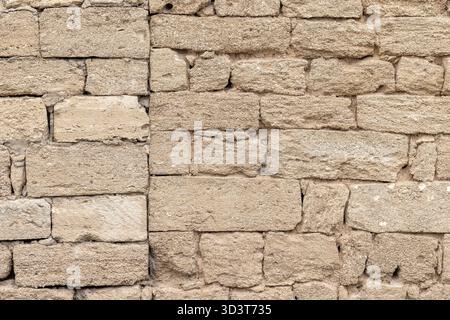 A textured shell rockwall made of irregular, weathered blocks in neutral beige and brown tones. This rugged exterior backdrop evokes historic masonry, Stock Photo